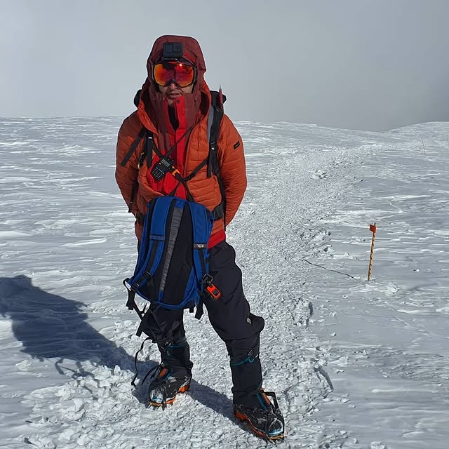 Instructor demonstrating winter mountaineering techniques on a snowy alpine mountain.